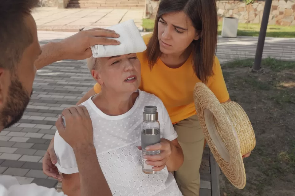 Two people helping an older woman outdoors suffering from heat stroke.